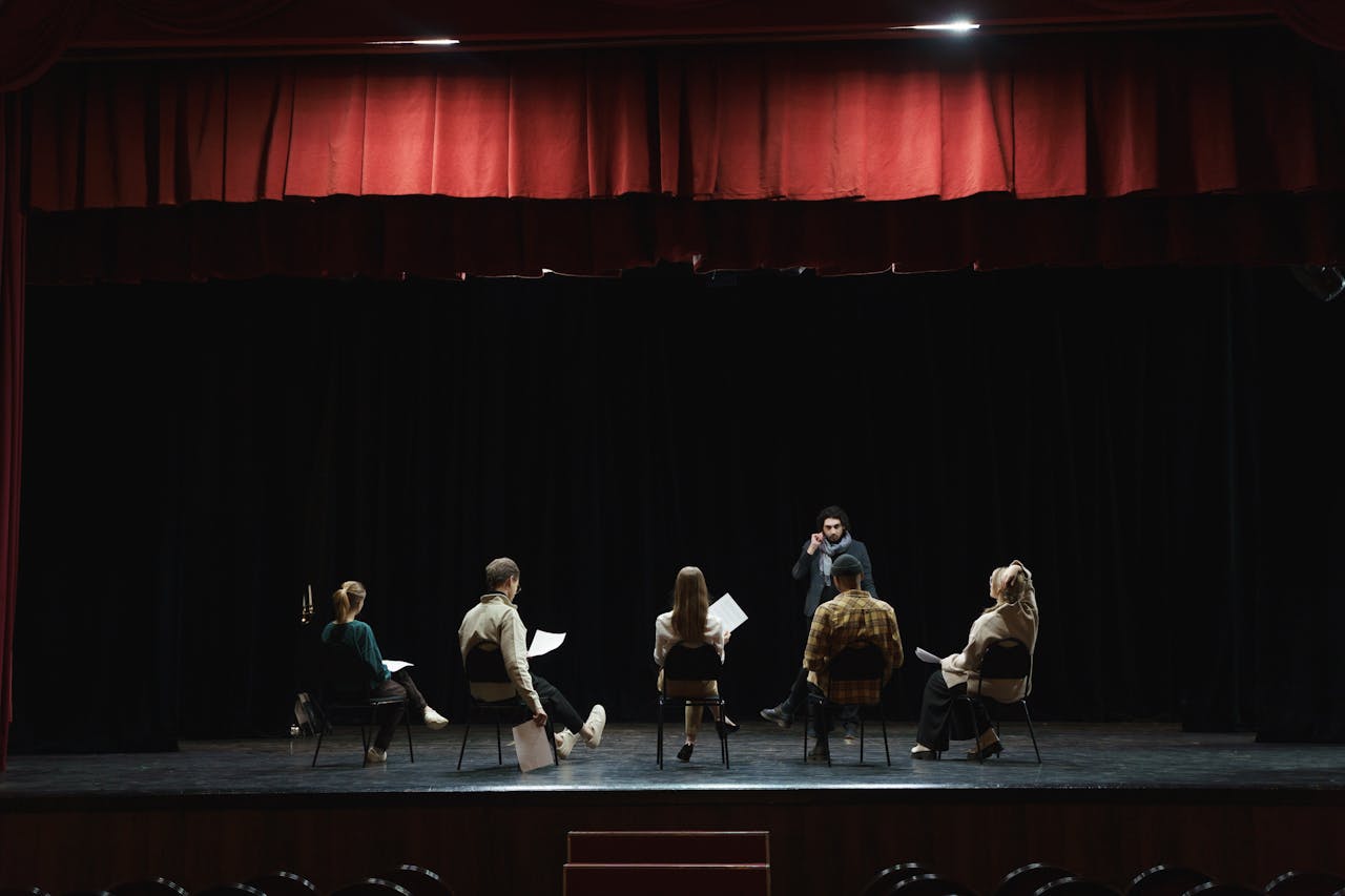 A group of actors rehearsing on a dimly lit stage in an auditorium, preparing for a theater performance.